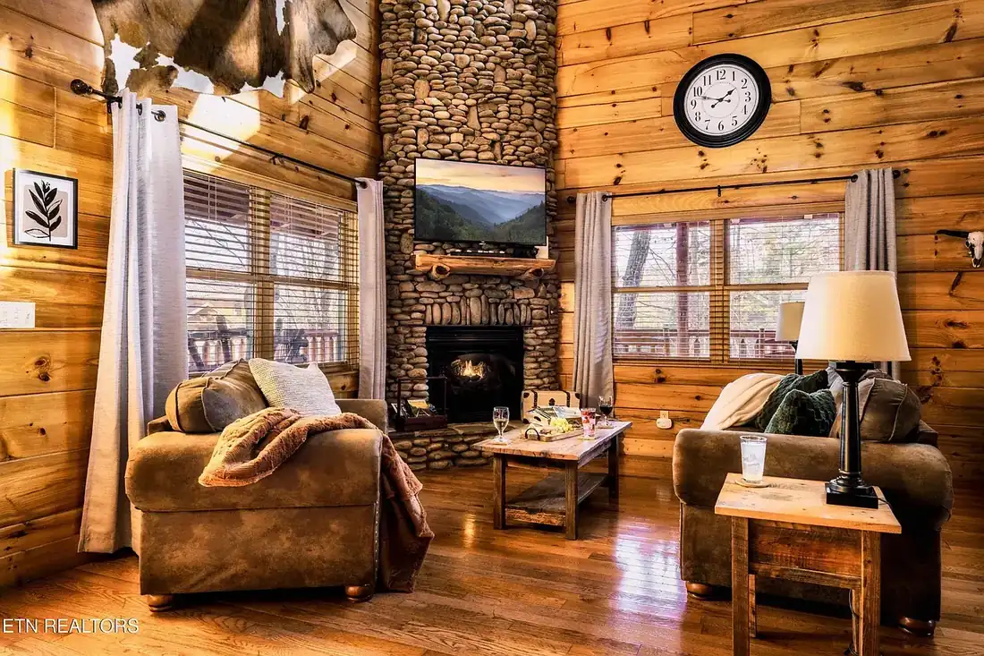 Floor-to-ceiling river rock fireplace with a lit fire and wall-mounted television above, flanked by two sofas on hardwood floors