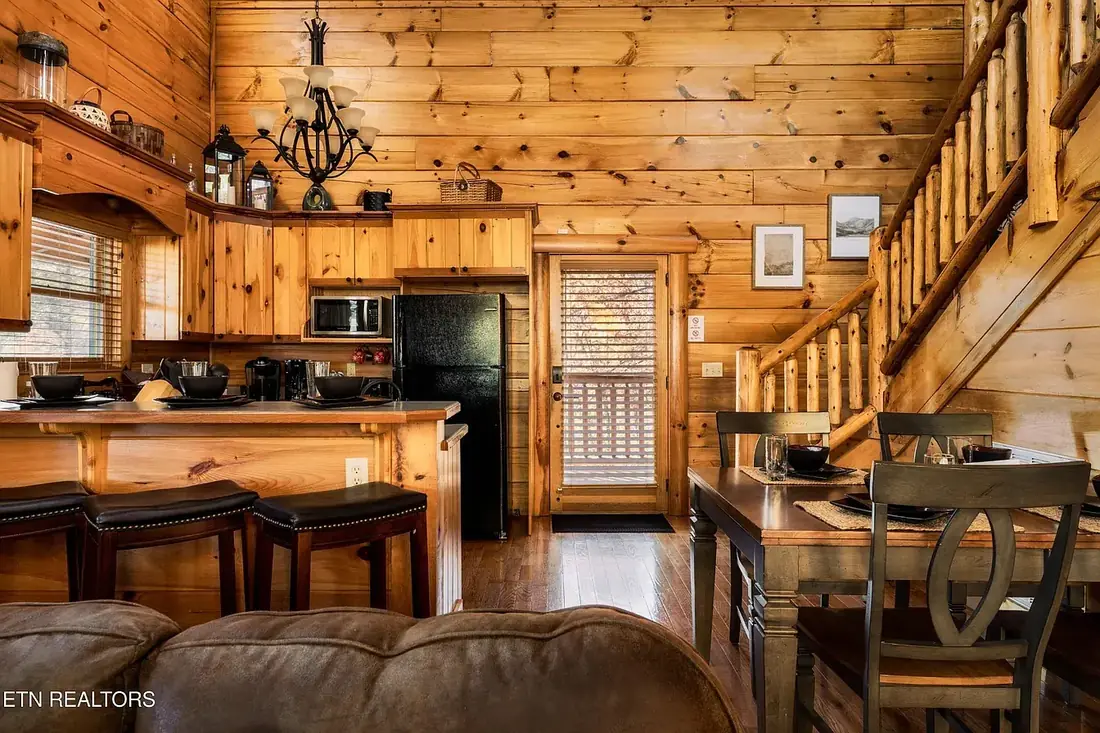 Kitchen with breakfast bar and three stools, full-size appliances, dining table for four, and the log staircase leading to the loft