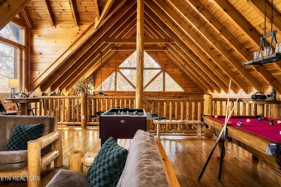 Loft game room open to the great room below, with log railing, exposed A-frame rafters, pool table and foosball table