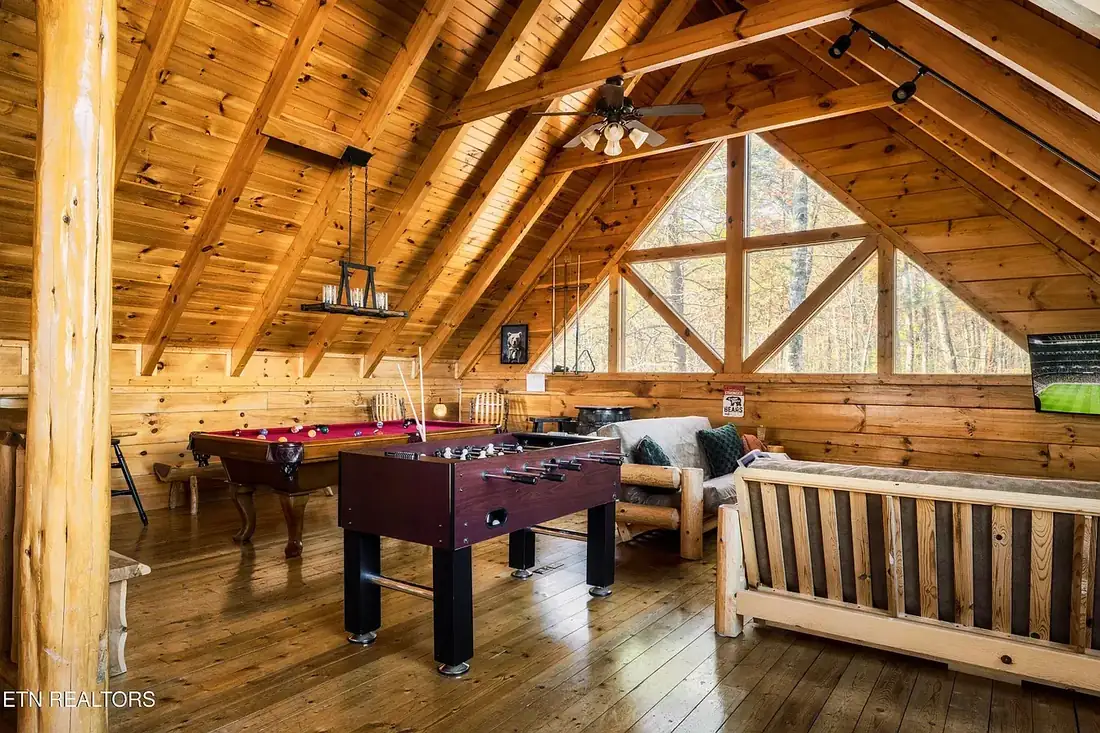 Game room under the A-frame roof with pool table, foosball table, futon sofa and a triangular gable window looking into the trees
