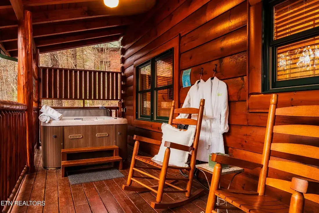 Hot tub on the covered deck with privacy screen, rocking chairs and robes hanging beside the cabin window