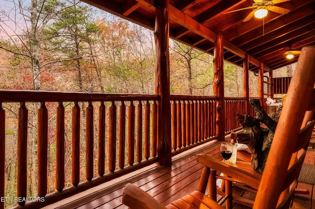 Covered deck with log railing, rocking chairs and ceiling fans, looking out into wooded autumn hillside at dusk
