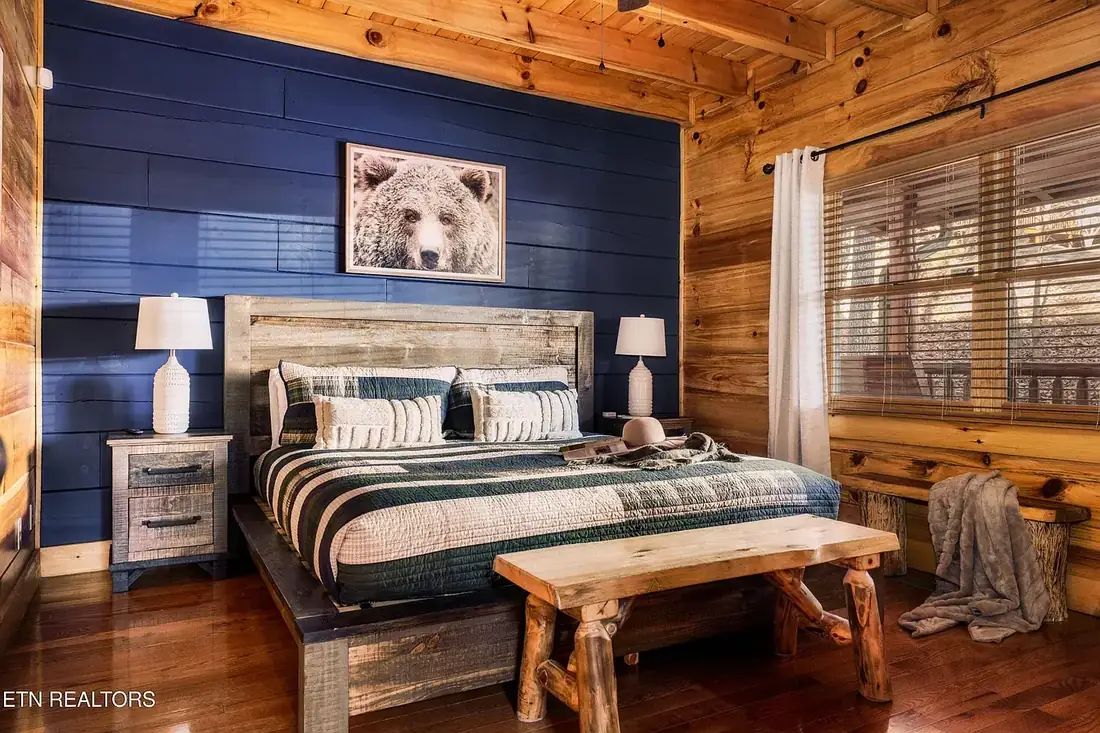 King bedroom with navy accent wall, framed bear photograph, reclaimed wood headboard and a log bench