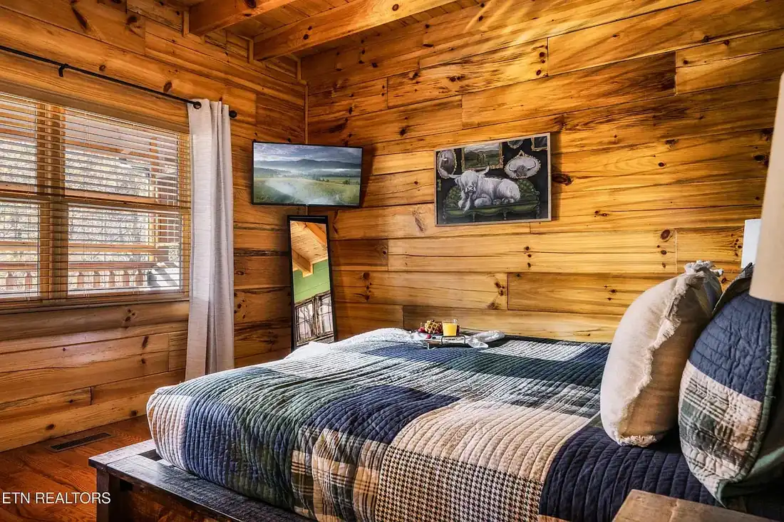 King bedroom with wall-mounted television, full-length mirror and windows looking onto the deck