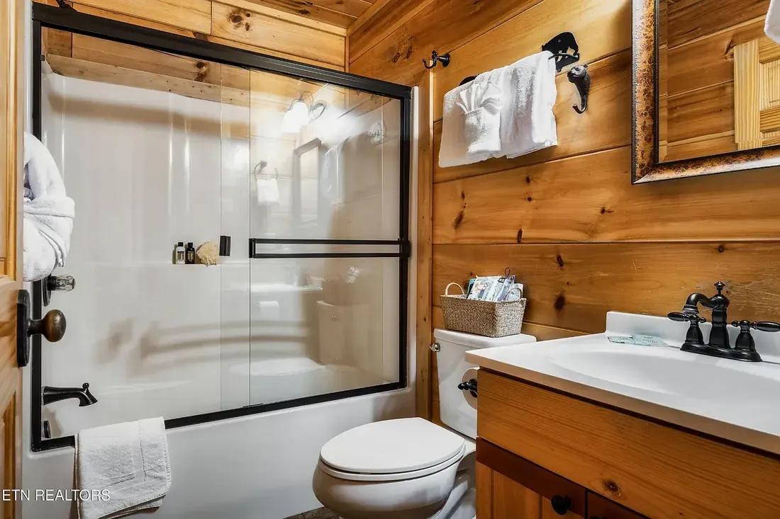 Full bathroom with tub and shower combination behind a glass door, vanity with black fixtures and wood plank walls